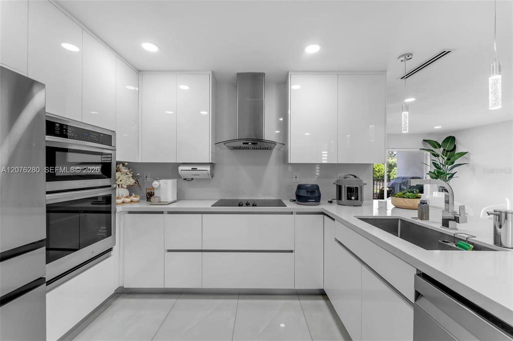 A modern kitchen features white flat-panel cabinetry, stainless steel appliances, and light-colored countertops — 1180 NW 124TH PLACE UNIT 208, MIAMI, FL
