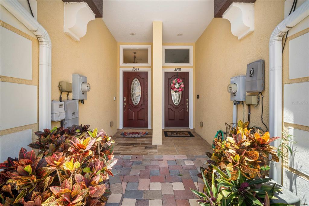 A paved walkway leads to two adjacent front doors with address numbers on a porch — 2974 ESTANCIA PLACE, CLEARWATER, FL