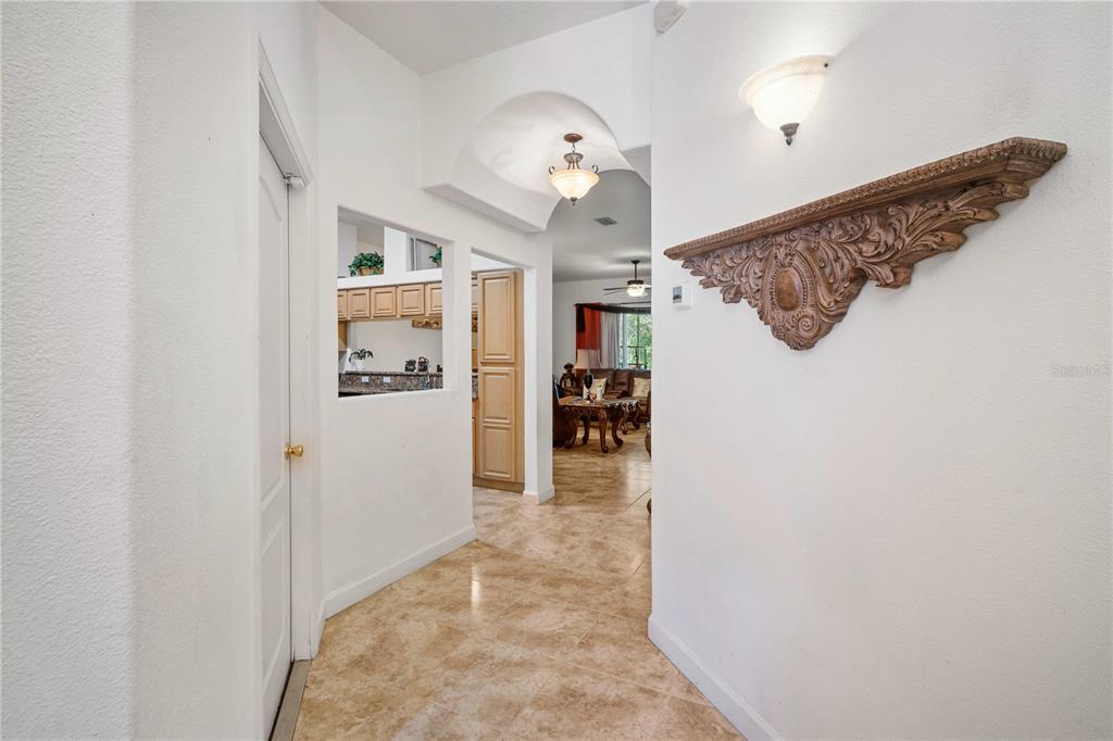 A hallway with tile flooring leads toward a living area, featuring a decorative wall shelf — 2974 ESTANCIA PLACE, CLEARWATER, FL