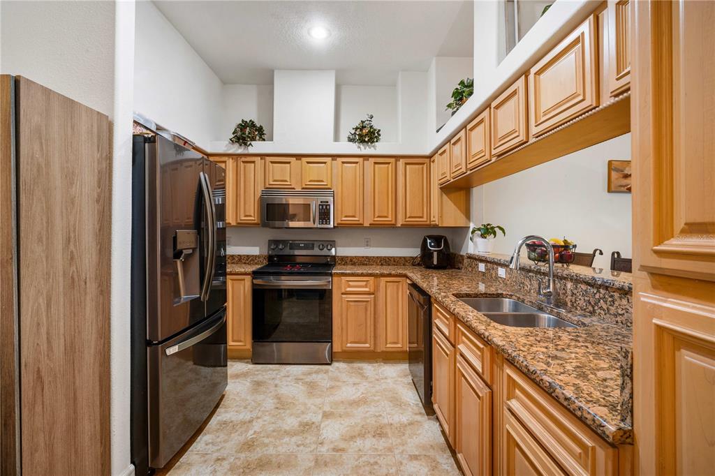 A kitchen features light wood cabinets, granite countertops, stainless steel appliances, and tile flooring — 2974 ESTANCIA PLACE, CLEARWATER, FL