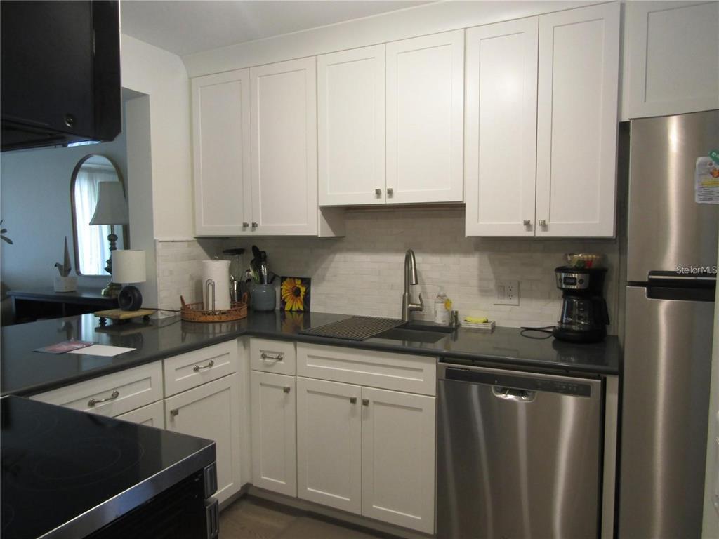 A kitchen features white cabinets, dark countertops, stainless steel appliances, and a tiled backsplash — 4516 LONGWATER UNIT 29, SARASOTA, FL