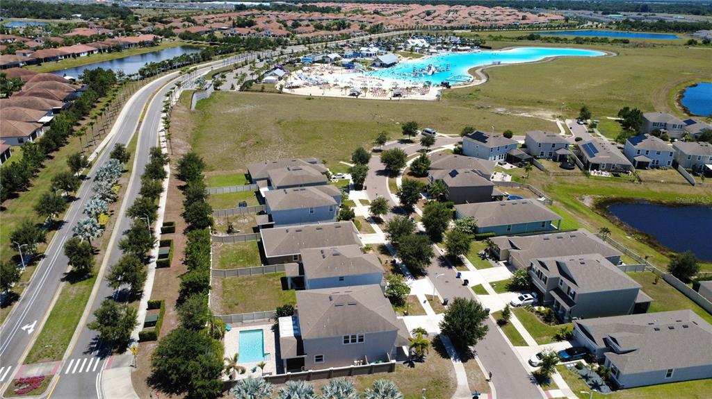 An aerial view shows suburban houses, a swimming pool, and a large recreational lagoon nearby — 5002 JACKEL CHASE DRIVE, WIMAUMA, FL