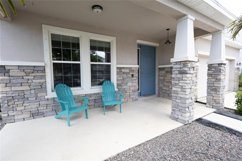 A covered front porch features stone veneer, two teal Adirondack chairs, and a blue door — 5002 JACKEL CHASE DRIVE, WIMAUMA, FL