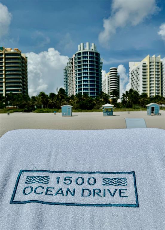 A white towel with a logo sits on a beach facing several tall coastal buildings — 1500 OCEAN DRIVE UNIT 905, MIAMI BEACH, FL