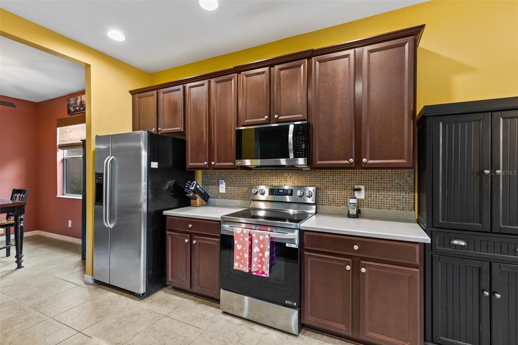 A kitchen features dark wood cabinets, stainless steel appliances, and a tiled backsplash — 2617 BRIGHTSIDE COURT, CAPE CORAL, FL