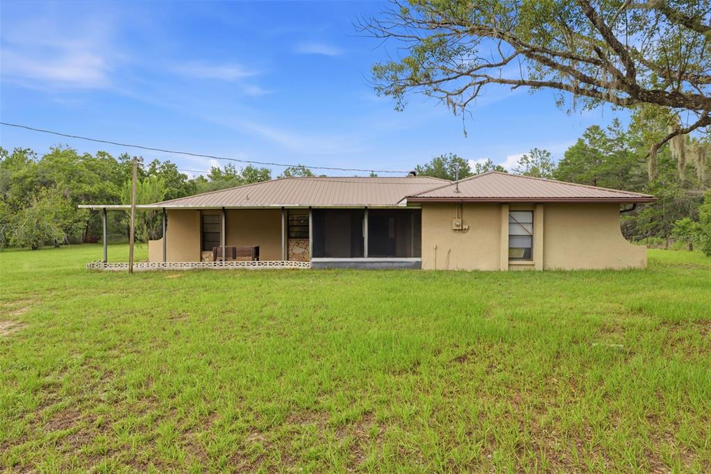 A single-story house with a metal roof and a screened-in porch sits on a lawn — 14499 SANDY DRIVE, BROOKSVILLE, FL