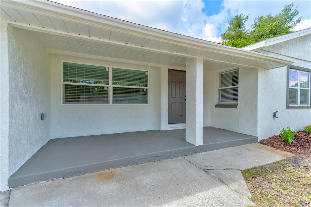 A white stucco house features a covered front porch, a brown door, and large windows — 47 DAHLIA DRIVE, DEBARY, FL