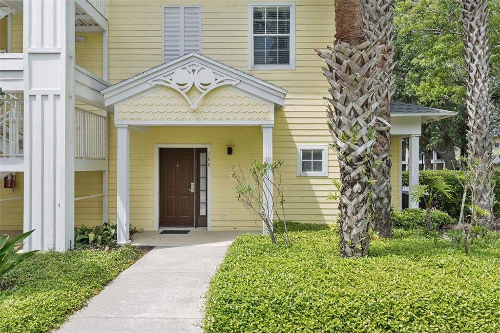A yellow building exterior features a covered entryway with a brown door and palm trees — 106 LUCAYA LOOP, DAVENPORT, FL