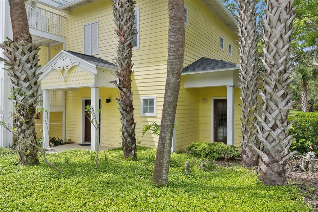 A yellow two-story house exterior features a covered porch, brown doors, and several palm trees — 106 LUCAYA LOOP, DAVENPORT, FL