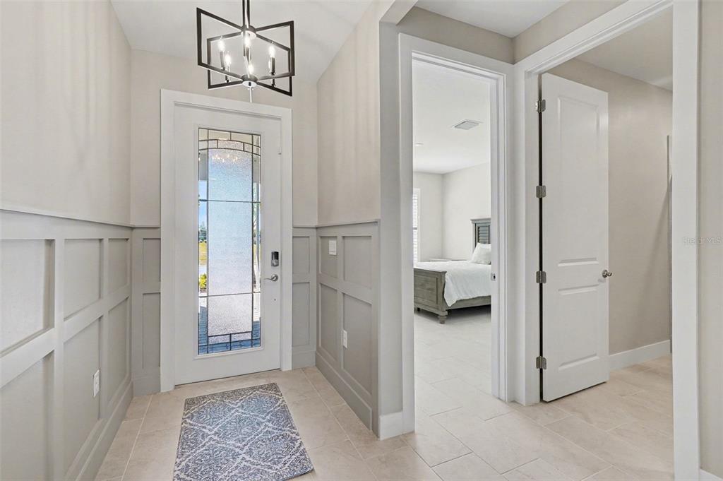 An entryway features wainscoting, a glass-paneled door, a geometric chandelier, and tile flooring — 44489 PANTHER DRIVE, PUNTA GORDA, FL