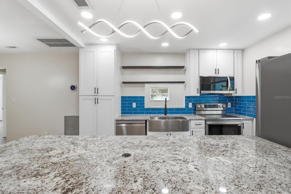 An open-concept living area features light wood-look flooring, a granite-topped kitchen island, and folding glass doors — 700 E STRATFORD ROAD, LECANTO, FL