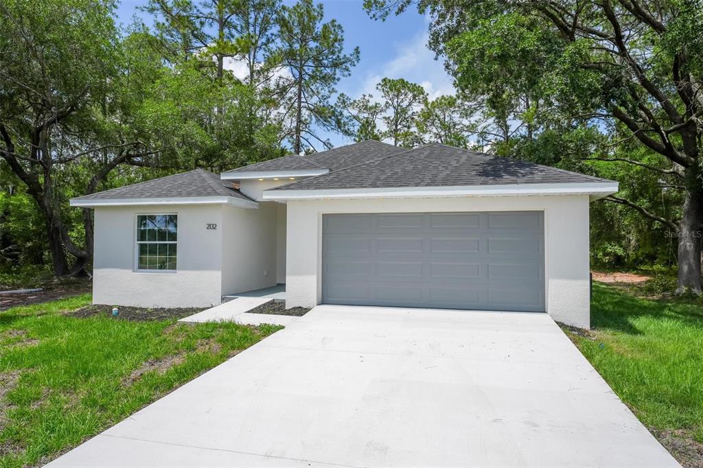 A single-story house with a white stucco exterior, a gray garage door, and a driveway — 2132 PINE MEADOWS GOLF COURSE ROAD, EUSTIS, FL