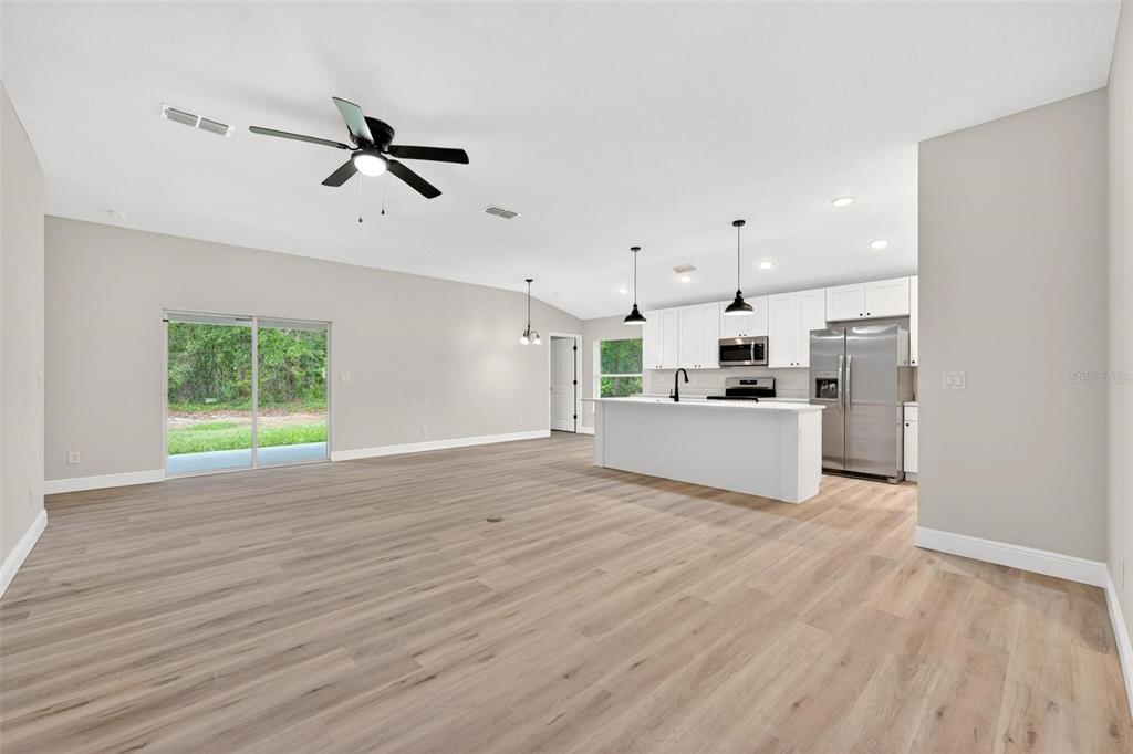 An open-concept living area features light wood flooring, a kitchen island, and sliding glass doors — 2132 PINE MEADOWS GOLF COURSE ROAD, EUSTIS, FL