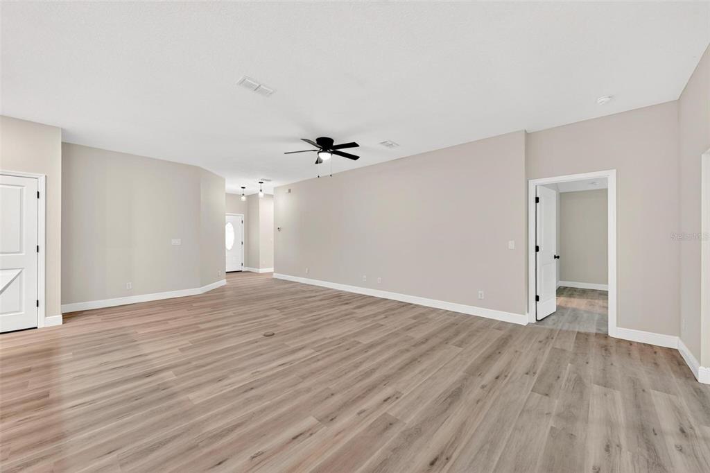 A spacious room features light wood-look flooring, neutral walls, a ceiling fan, and white doors — 2132 PINE MEADOWS GOLF COURSE ROAD, EUSTIS, FL