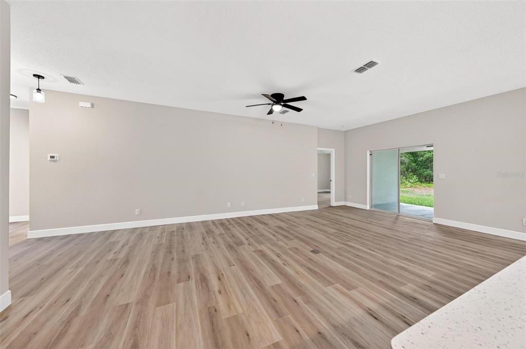 A spacious living room features light wood-look flooring, a ceiling fan, and sliding glass doors — 2132 PINE MEADOWS GOLF COURSE ROAD, EUSTIS, FL