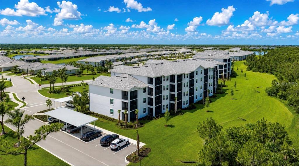 An aerial view of a multi-story apartment building with a covered parking lot and lawn — 14191 HERITAGE LANDING BOULEVARD UNIT 1214, PUNTA GORDA, FL