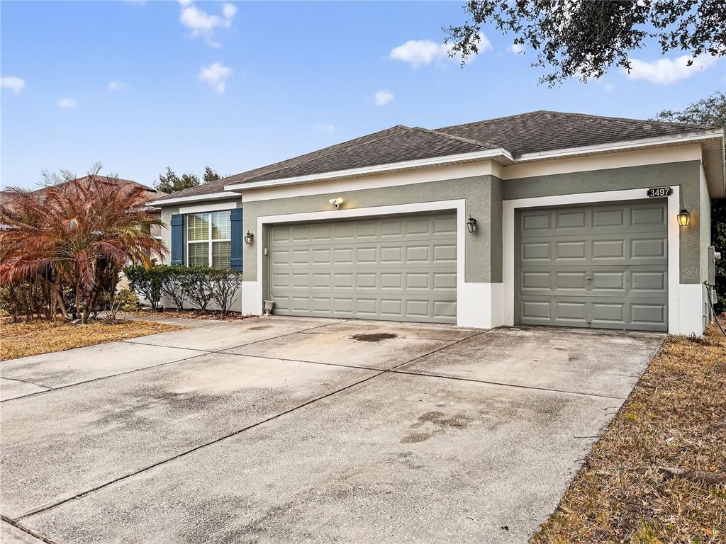 A single-story house exterior features a three-car garage, a concrete driveway, and a palm tree — 3497 BUNCHBERRY WAY, OCOEE, FL