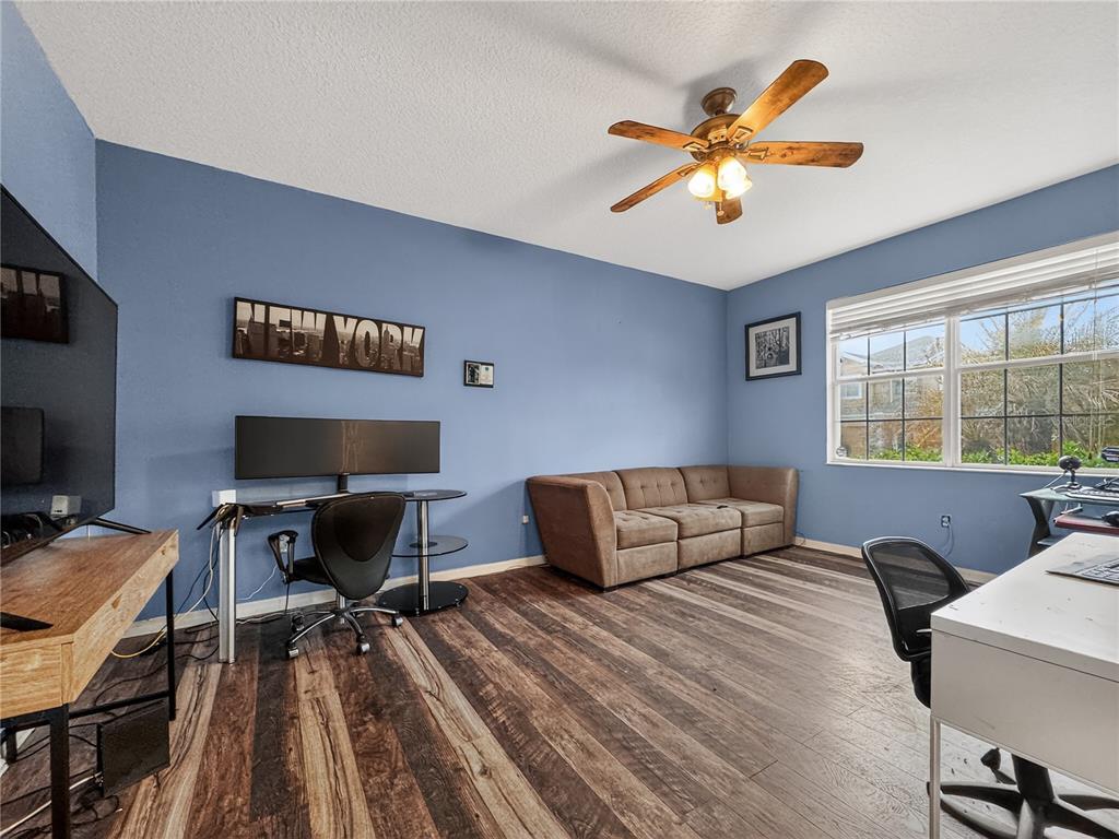 A blue-walled home office features wood-look flooring, a brown sofa, and two computer desks — 3497 BUNCHBERRY WAY, OCOEE, FL