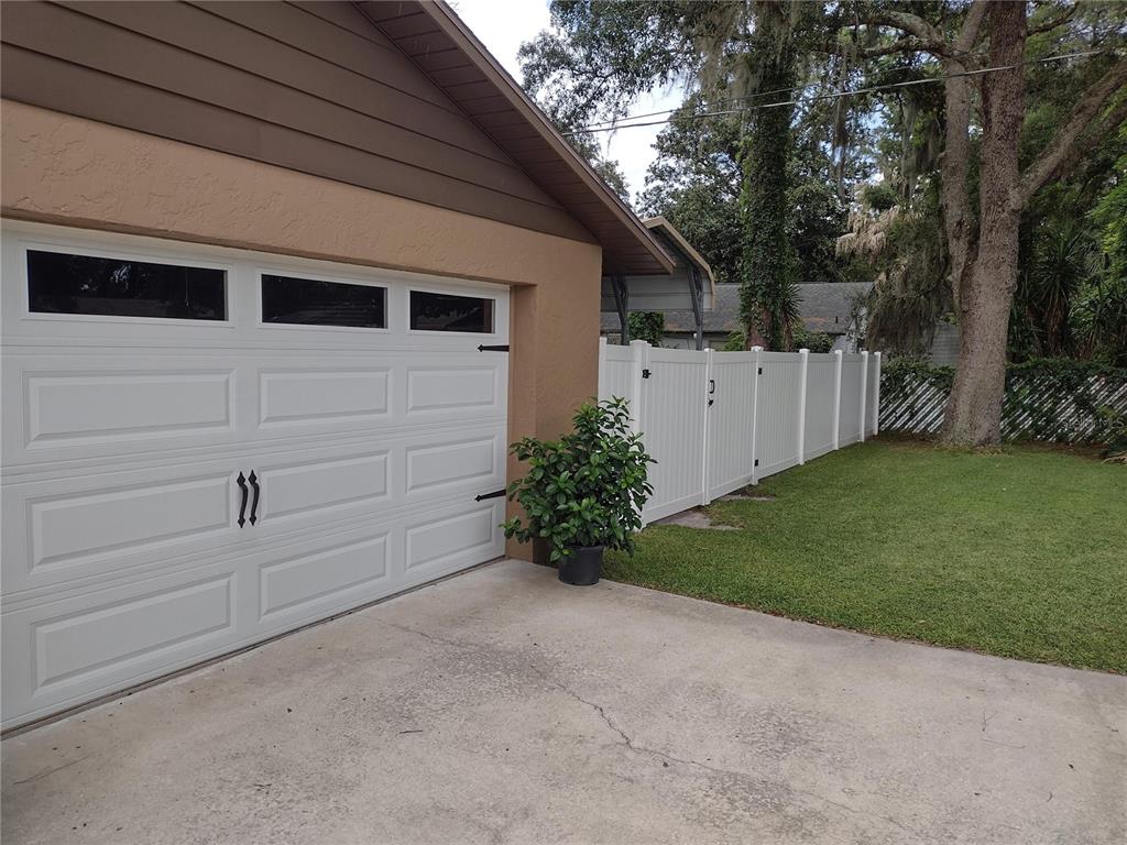 A white garage door and a white vinyl fence border a concrete driveway and lawn — 2301 NE 32ND PLACE, OCALA, FL