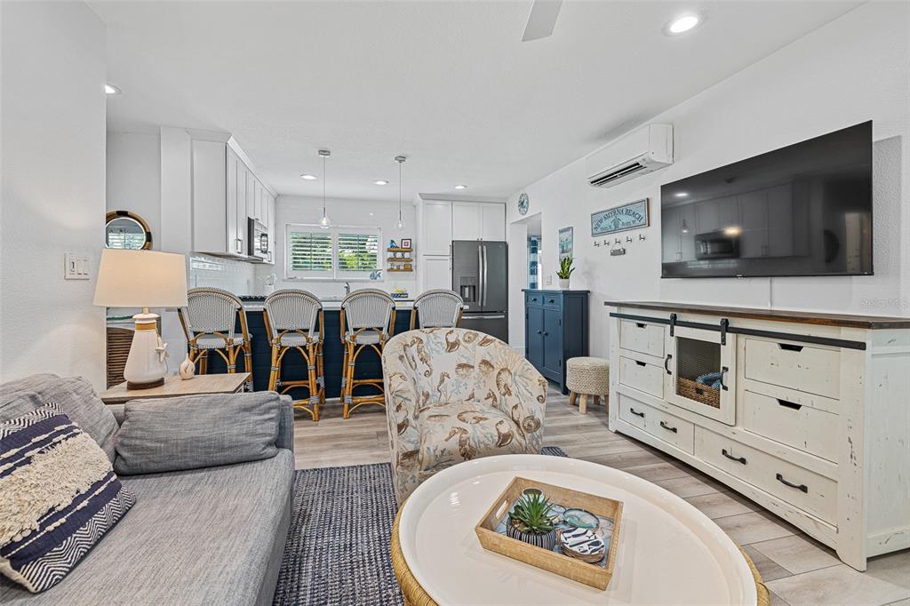 A living room with a gray sofa, patterned armchair, white media console, and open kitchen — 839 E 10TH AVENUE, NEW SMYRNA BEACH, FL