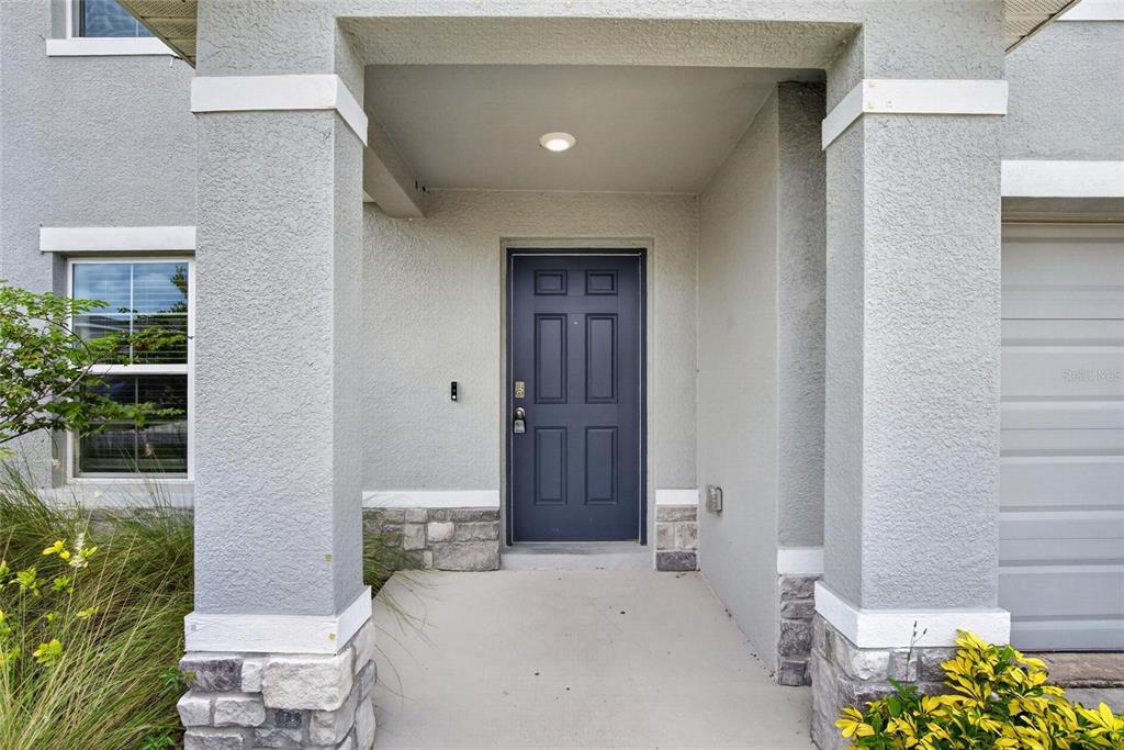 A covered entryway features a dark blue front door, gray stucco walls, and stone accents — 2818 GUMBO LIMBO DRIVE, WIMAUMA, FL