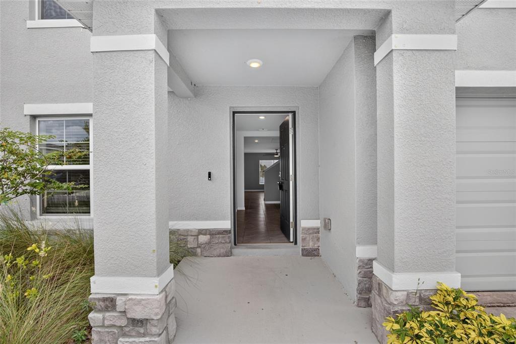 A covered entryway with stone-accented columns leads to an open front door — 2818 GUMBO LIMBO DRIVE, WIMAUMA, FL
