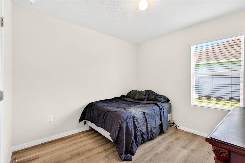 A bedroom with light walls, wood-look flooring, a bed with dark bedding, and a window — 55 HICKORY COURSE, OCALA, FL