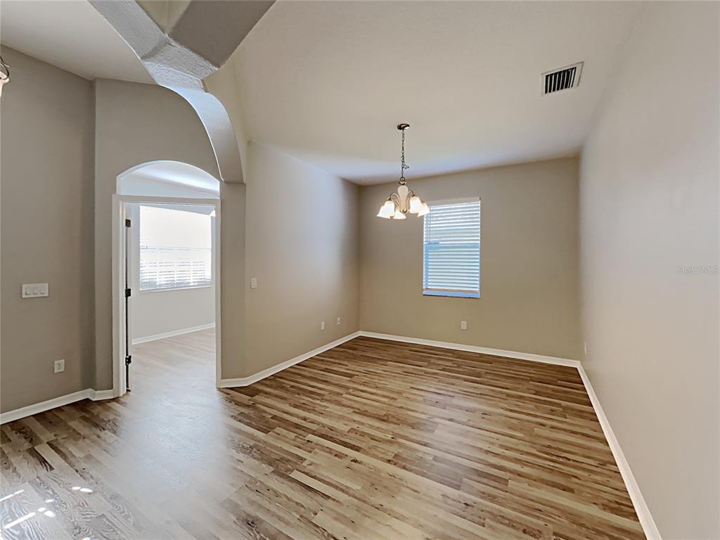 An empty dining room features wood-look flooring, a chandelier, and an arched entryway — 4020 LANGDRUM DRIVE, WESLEY CHAPEL, FL