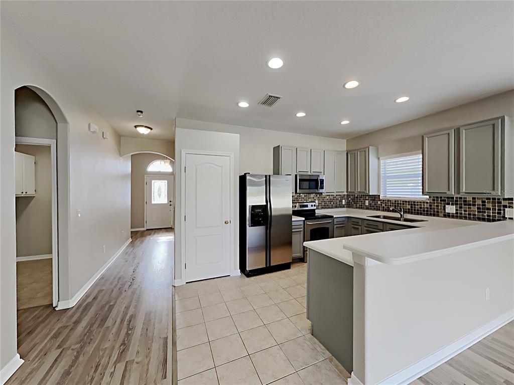 A kitchen with gray cabinets, stainless steel appliances, and tile flooring opens to a hallway — 4020 LANGDRUM DRIVE, WESLEY CHAPEL, FL