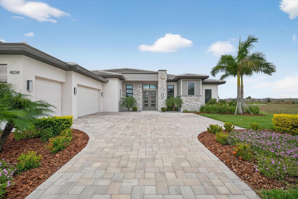 A single-story house with a stone facade, gray roof, and a paved driveway near water — 4034 BUTTE TRAIL, BRADENTON, FL