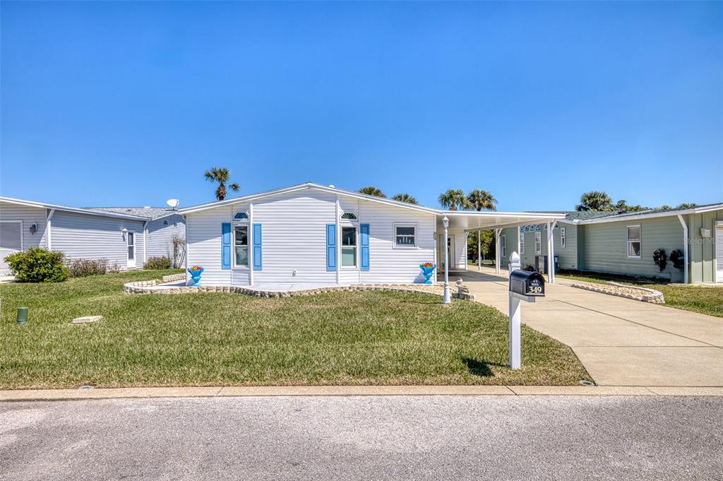 A white manufactured home with blue shutters and a carport sits on a grassy lot — 349 MARSH LANDING LOOP, OAK HILL, FL