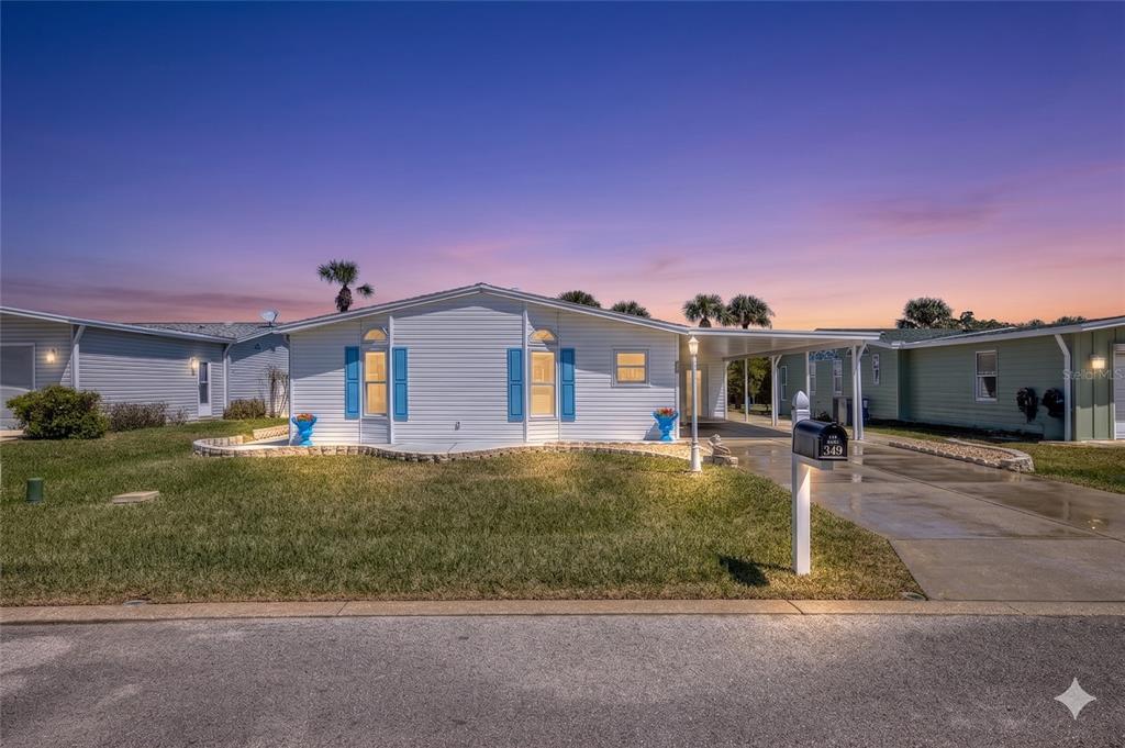 A white single-story house with blue shutters and a carport sits behind a grassy lawn — 349 MARSH LANDING LOOP, OAK HILL, FL
