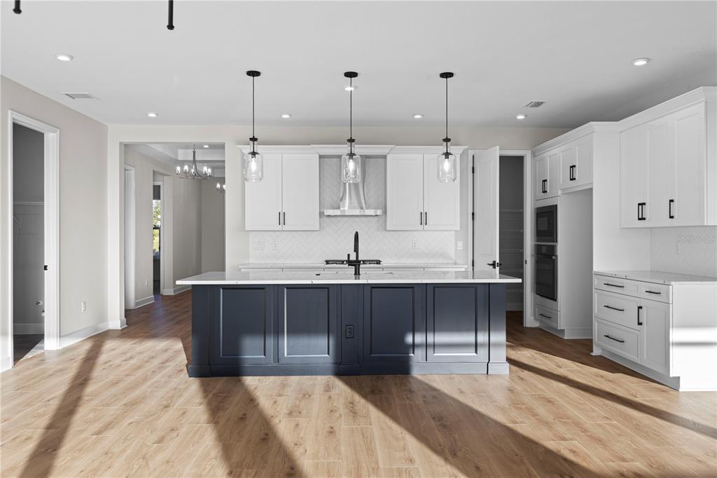 A modern kitchen features a dark blue island, white cabinets, and light wood flooring — 1617 BELLAGIO LOOP, TAVARES, FL