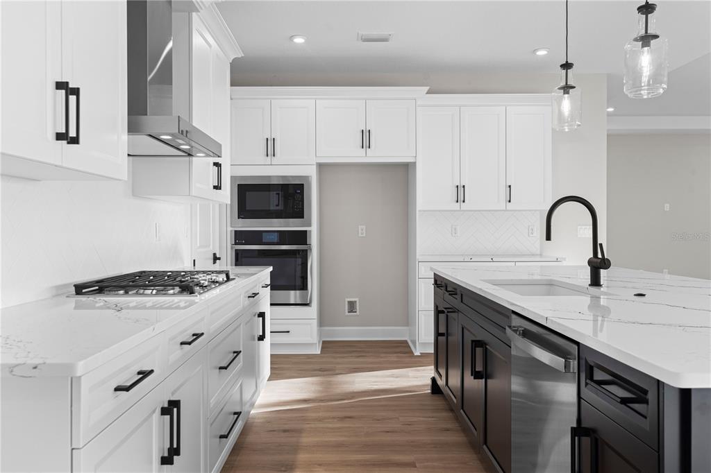 A modern kitchen features white cabinets, a dark island, stainless appliances, and quartz countertops — 1617 BELLAGIO LOOP, TAVARES, FL