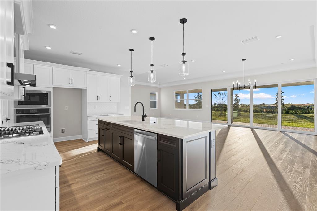A kitchen features a dark wood island, white cabinets, stainless steel appliances, and large windows — 1617 BELLAGIO LOOP, TAVARES, FL