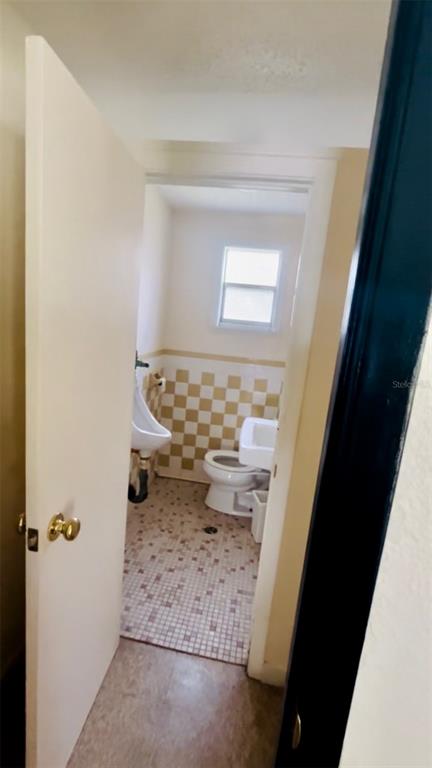 A bathroom features a toilet, a wall-mounted urinal, and a checkered tile wall — 7103 N CARL G ROSE HIGHWAY, HERNANDO, FL
