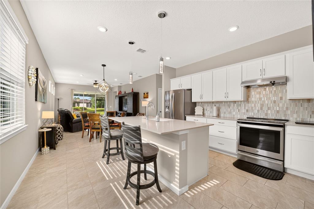 A modern kitchen with white cabinets, a central island, and tile flooring, opening to a dining area — 9664 SW 63RD LOOP, OCALA, FL