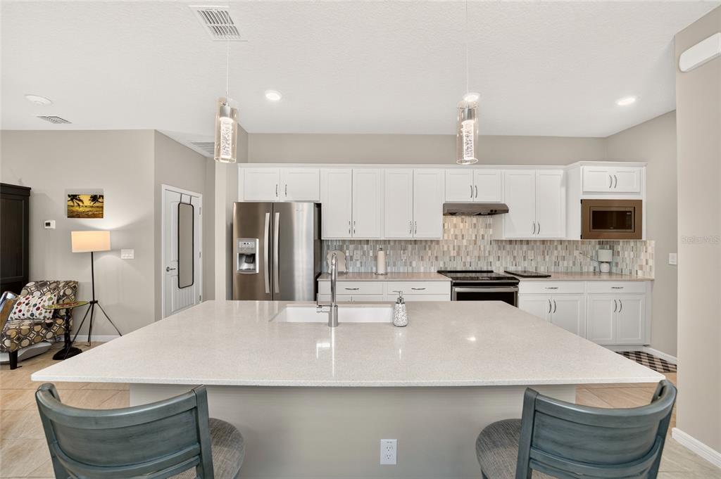 A kitchen features white cabinets, a large quartz island with a sink, and stainless appliances — 9664 SW 63RD LOOP, OCALA, FL