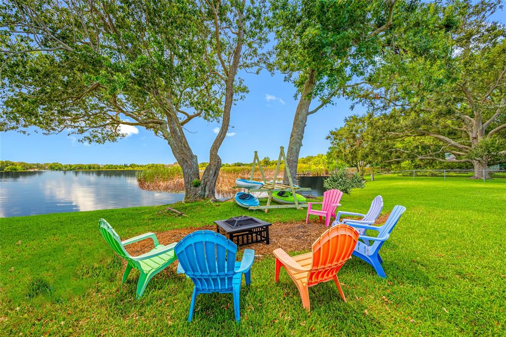 A fire pit area with colorful Adirondack chairs sits on a lawn by a lake — 2153 KARAN WAY, CLEARWATER, FL