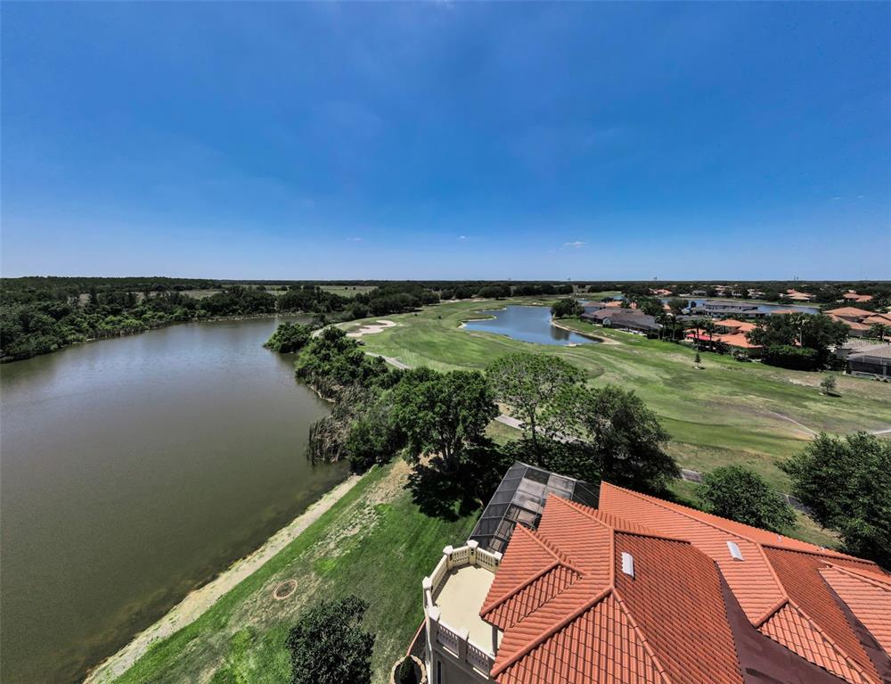 An aerial view shows a house with a tiled roof overlooking a lake and golf course — 10706 RUFFINO COURT, TRINITY, FL