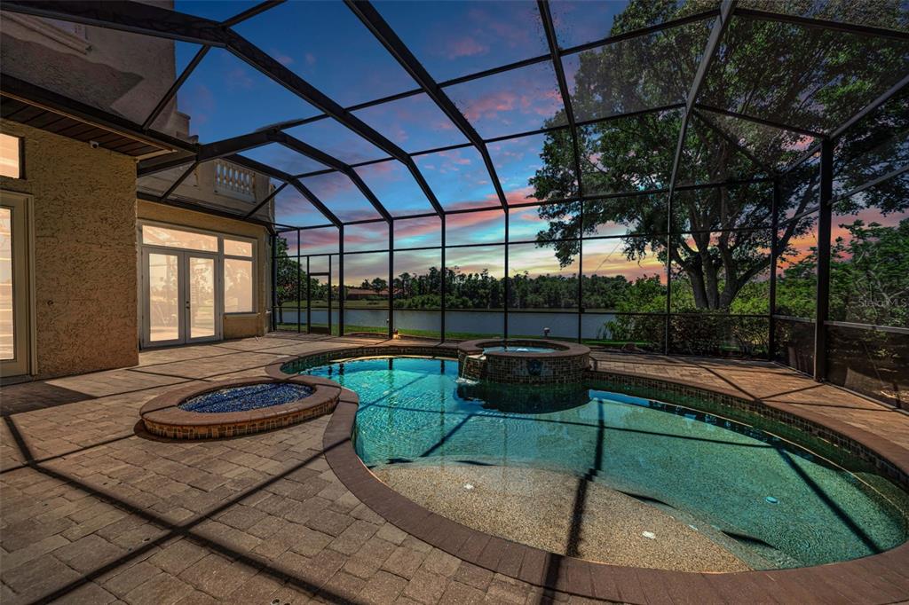 A screened-in patio features a swimming pool, a raised spa, and views of a lake — 10706 RUFFINO COURT, TRINITY, FL