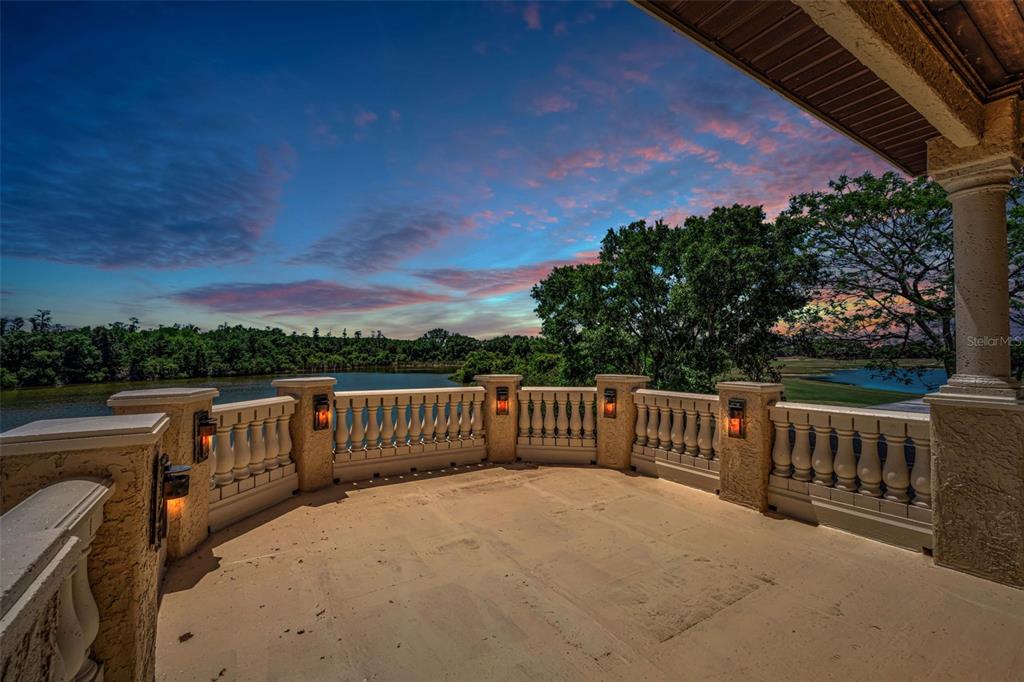 A stone balcony with a balustrade railing overlooks a lake at sunset — 10706 RUFFINO COURT, TRINITY, FL