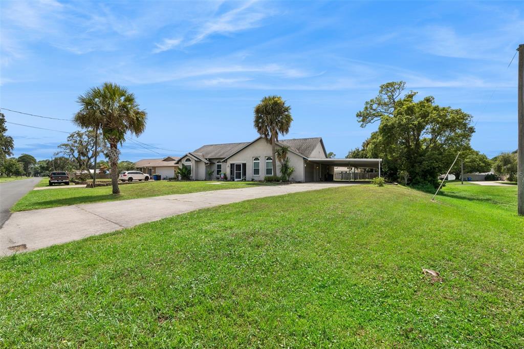 A single-story house with a concrete driveway, a carport, and palm trees on a grassy lot — 2504 GLENWOOD DRIVE, EDGEWATER, FL