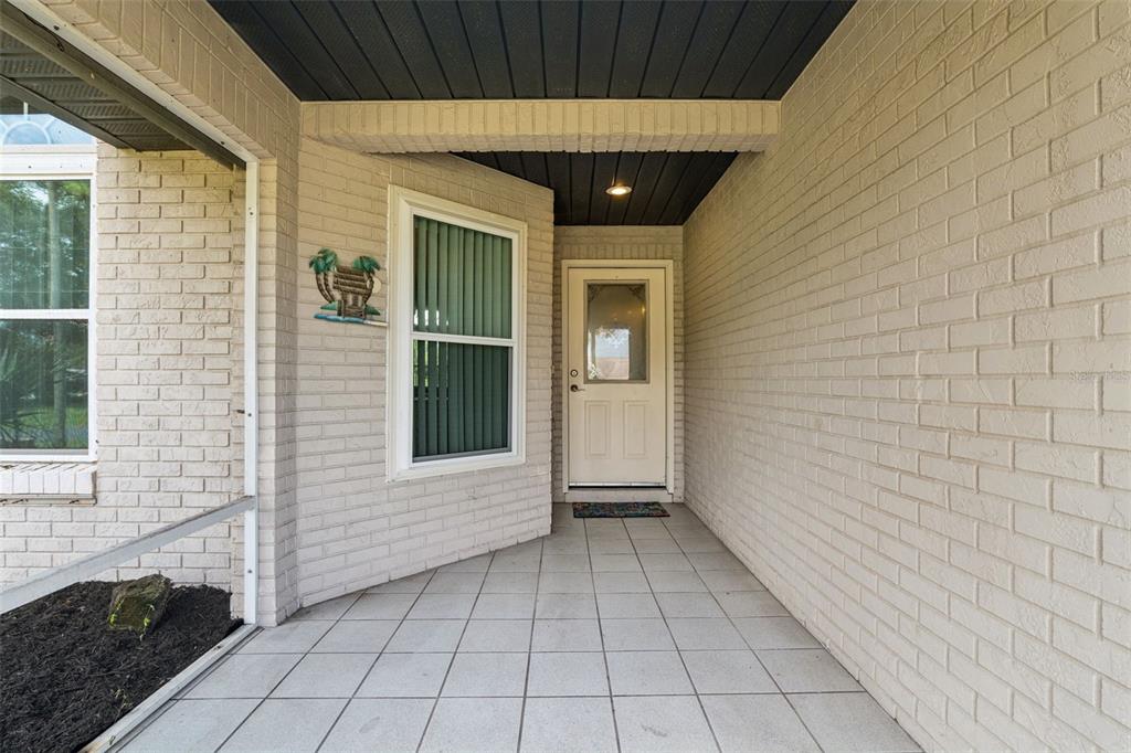 A covered brick entryway features a tiled floor, a white front door, and a window — 2504 GLENWOOD DRIVE, EDGEWATER, FL
