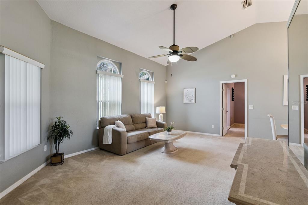 A living room features a tan sofa, vaulted ceilings, a ceiling fan, and arched windows — 2504 GLENWOOD DRIVE, EDGEWATER, FL