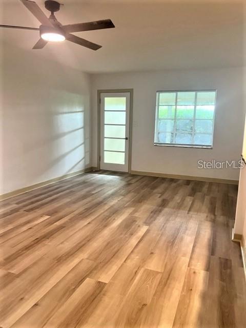 An empty room features light wood-look flooring, a ceiling fan, a glass-paneled door, and windows — 2185 FLORENCE ROAD, MOUNT DORA, FL