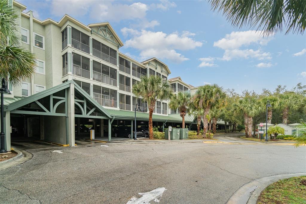 A multi-story apartment building features screened balconies and a covered ground-level parking area — 14200 AVALON ROAD UNIT 406, WINTER GARDEN, FL