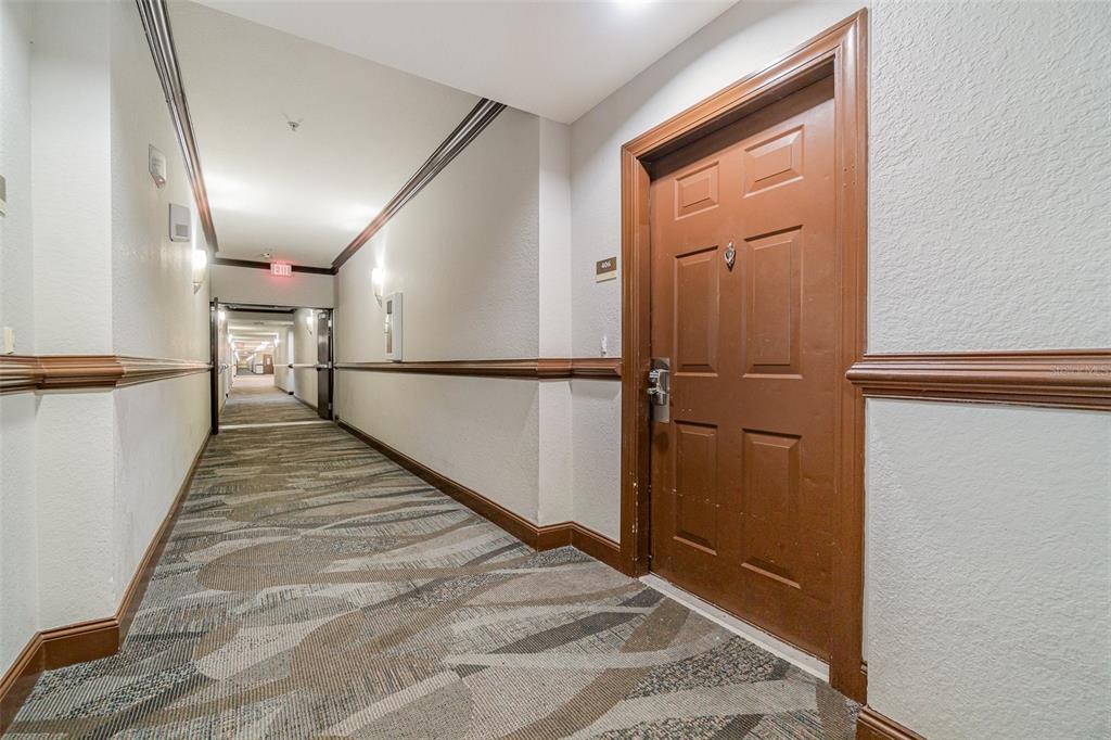 A brown door with a metal handle stands in a carpeted hotel-style hallway — 14200 AVALON ROAD UNIT 406, WINTER GARDEN, FL