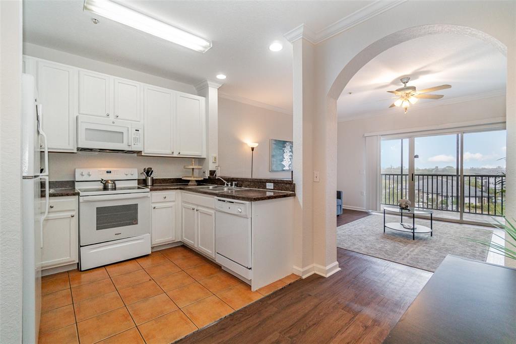 A kitchen with white cabinets and tile flooring opens into a living area with balcony access — 14200 AVALON ROAD UNIT 406, WINTER GARDEN, FL