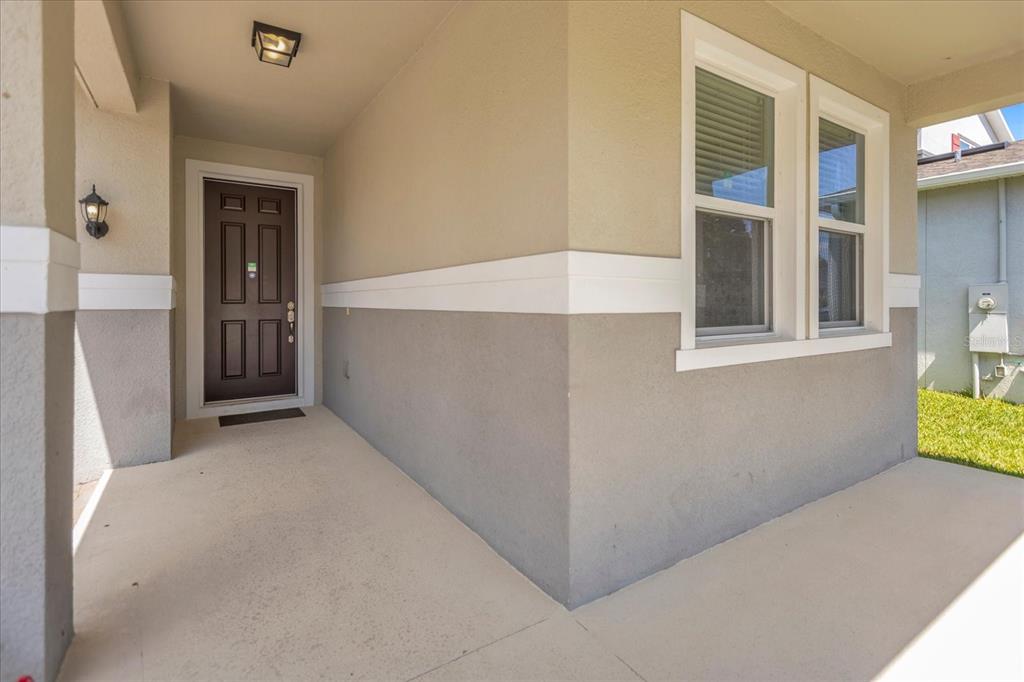 A covered front porch features a dark brown door and light-colored stucco walls — 8060 BOWERY DRIVE, WINTER GARDEN, FL